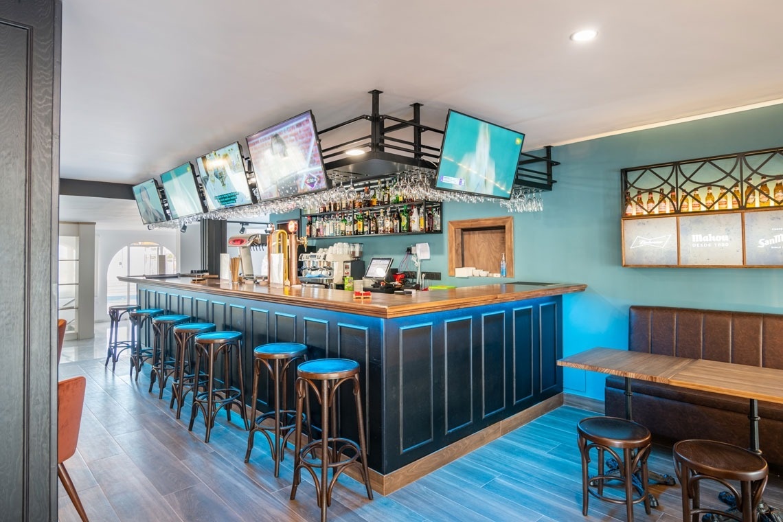 un bar con muchos televisores y un letrero de mahou en la pared