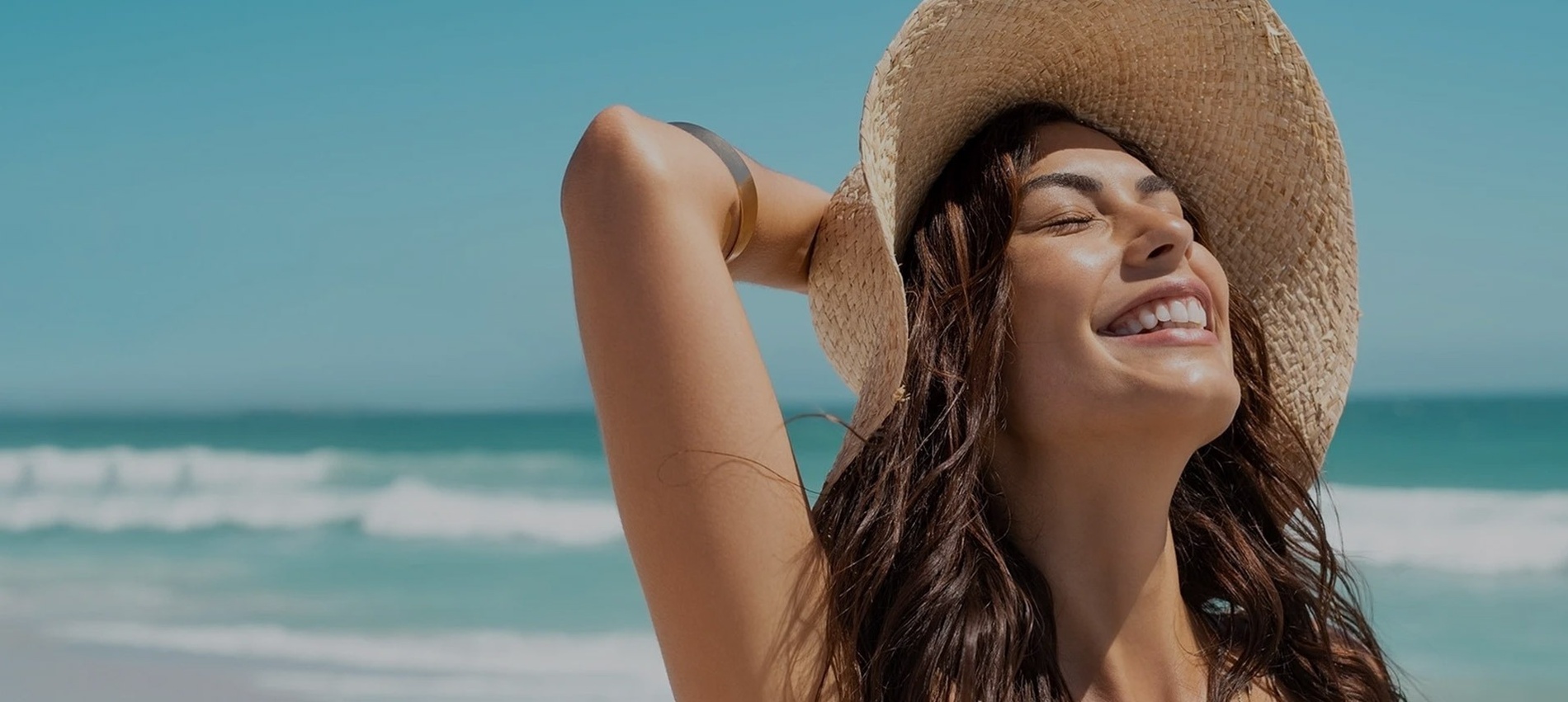 a woman wearing a straw hat is smiling on the beach