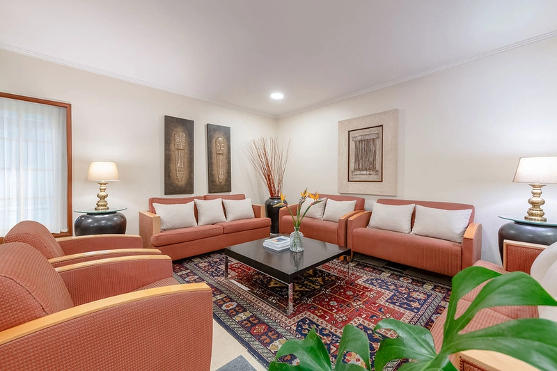 Salón de hotel con sillones y sofá color orquídea, mesa de centro y arte moderno.