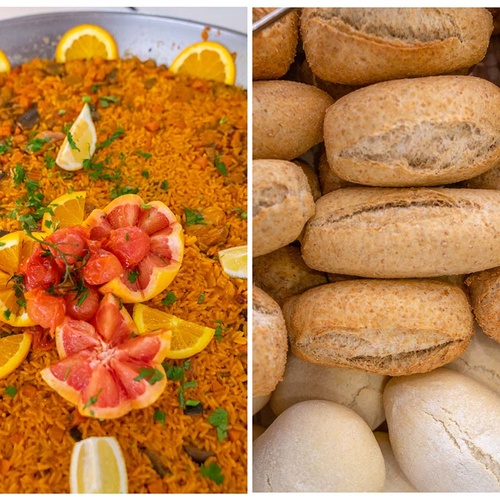 En la imagen se ve una paella grande decorada con cítricos a la izquierda y un montón de panecillos variados a la derecha.