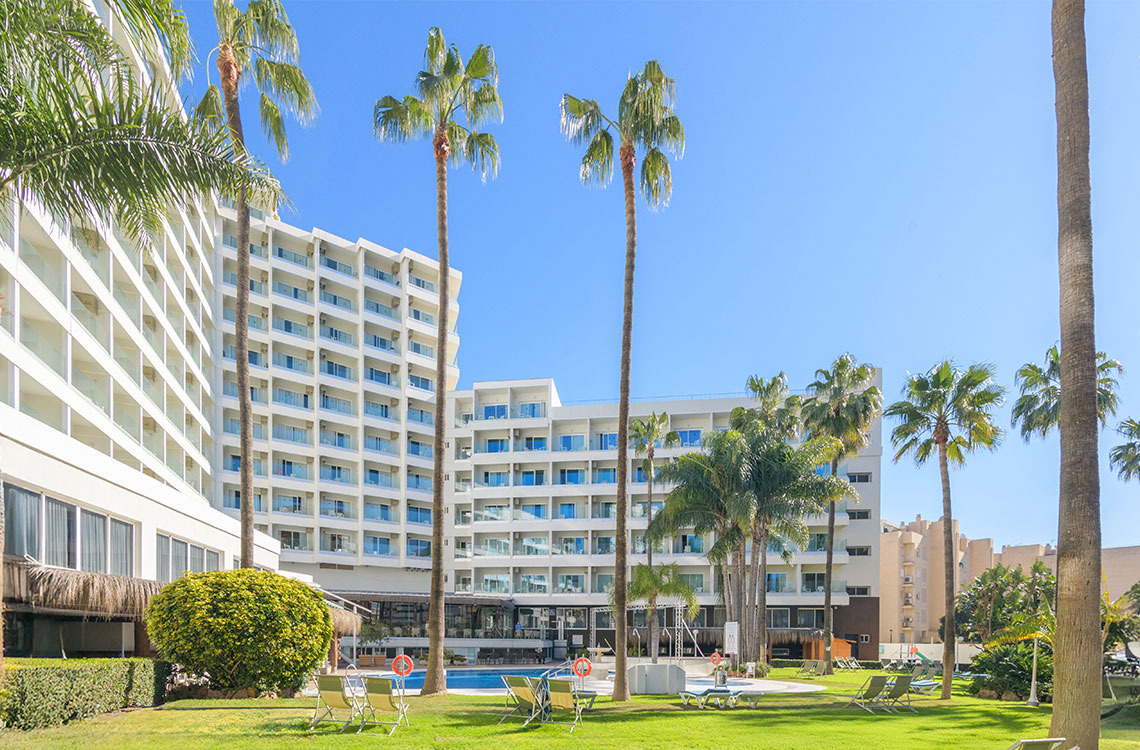 Resort with palm trees, pool, and white hotel buildings. Dorobe: Parasol vacation.