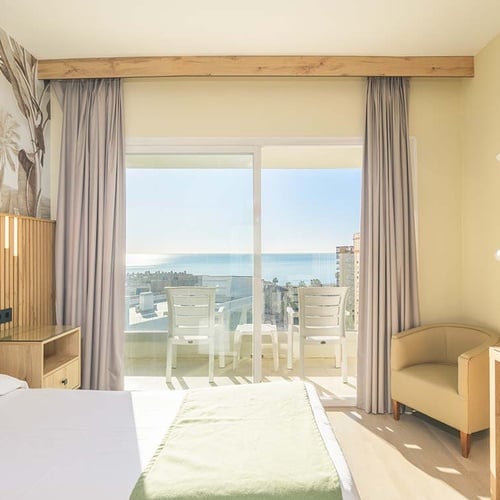 Habitación de hotel luminosa y moderna con una cama, balcón y vistas al mar.