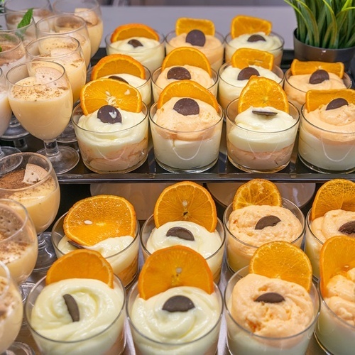 a variety of desserts in small glasses with orange slices on top