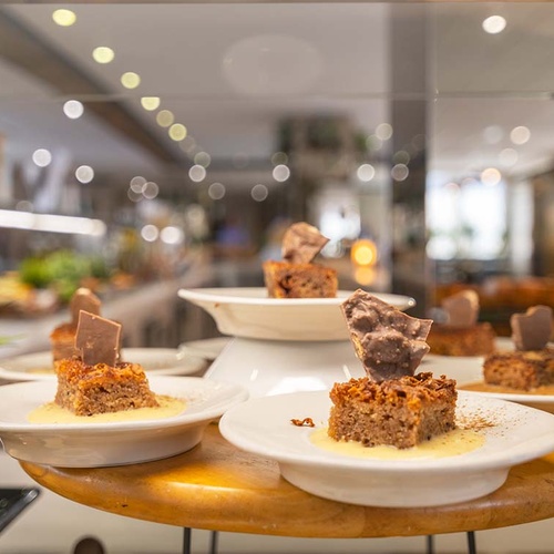 Pequeñas porciones individuales de postre con natillas y trozos de chocolate se exhiben en platos blancos sobre un mostrador de madera.