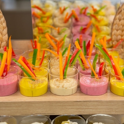 a variety of dips and vegetables in small glasses on a table