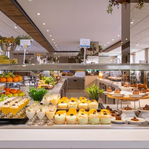 Una mesa de bufet bien surtida con una gran variedad de postres y frutas frescas se exhibe en un restaurante moderno y luminoso.