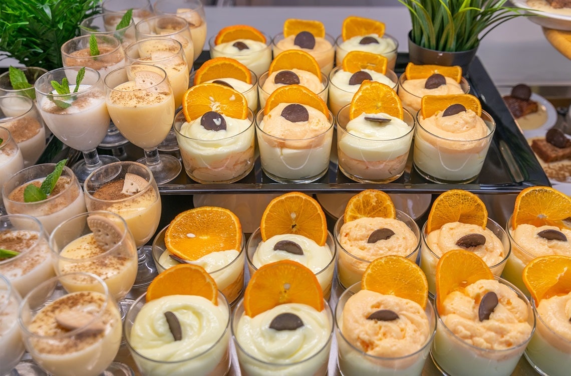 a variety of desserts in small glasses with orange slices on top