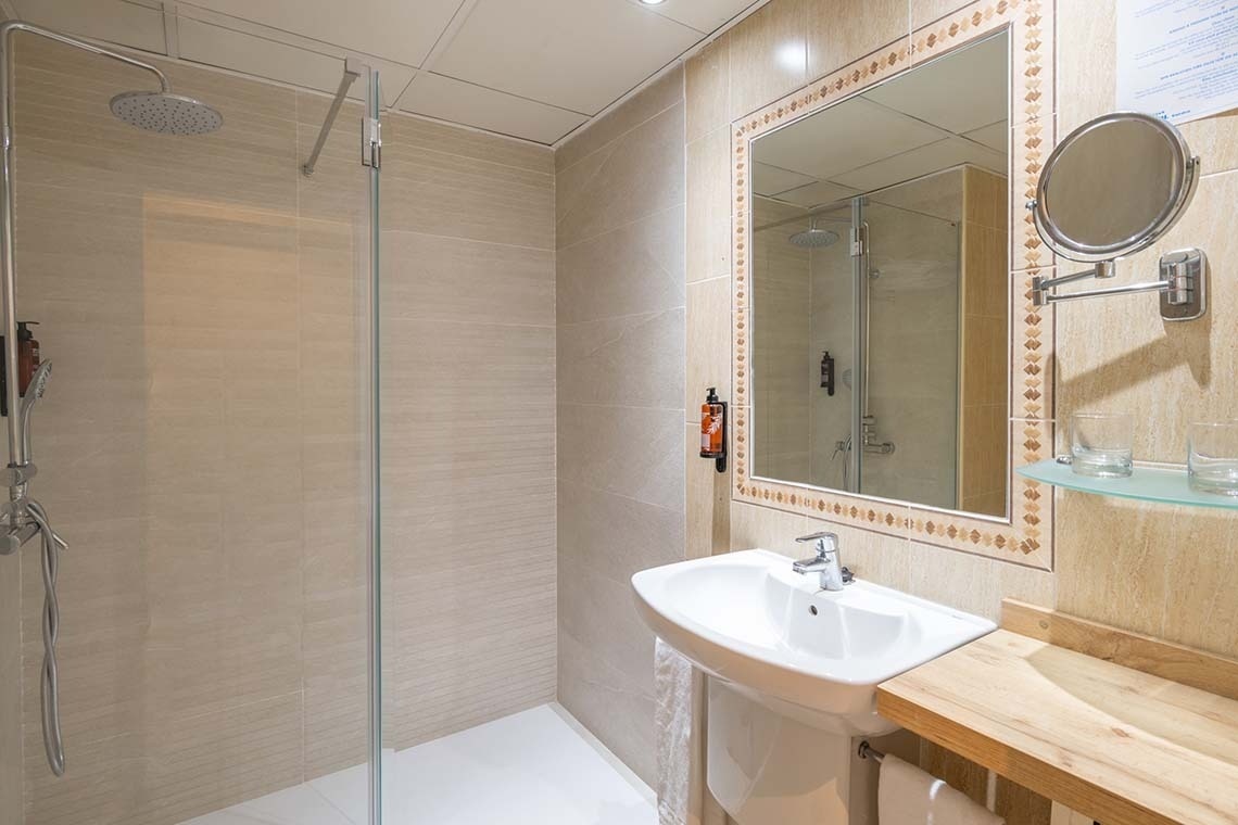 Un baño moderno y luminoso con ducha acristalada, lavabo y un gran espejo decorado sobre una pared de azulejos claros.