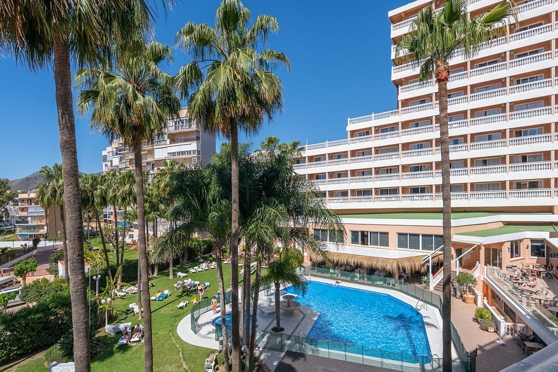 una gran piscina rodeada de palmeras frente a un hotel