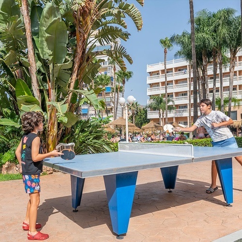 two children are playing ping pong in front of a hotel