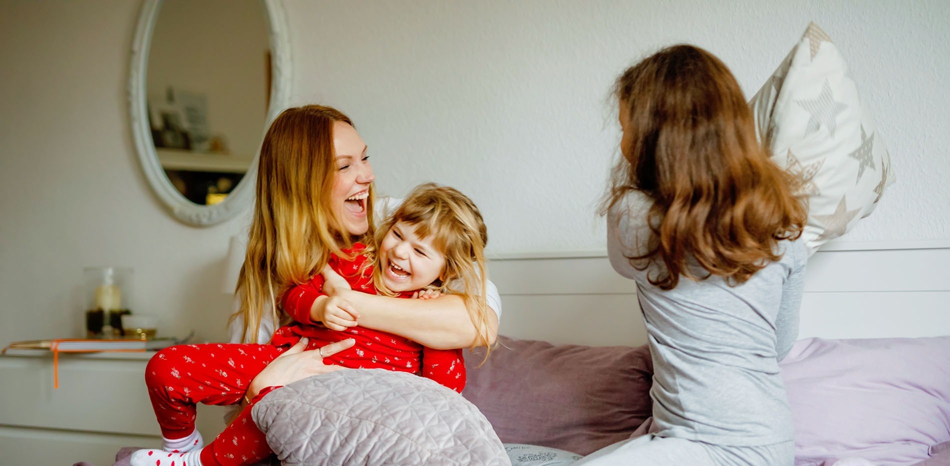 a woman and two girls are having a pillow fight on a bed