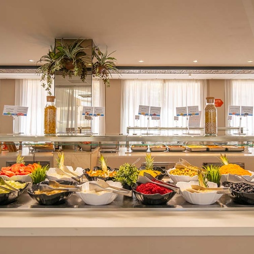Un luminoso y variado buffet presenta una amplia selección de ensaladas frescas y otros alimentos servidos en cuencos y un expositor de cristal.