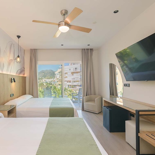 Esta moderna habitación de hotel dispone de dos camas, un balcón con vistas a la ciudad y la montaña, una televisión de pared y un ventilador de techo.