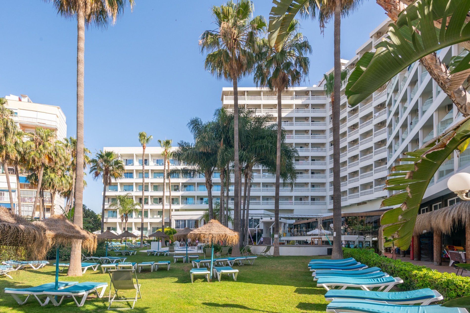 un gran edificio blanco está rodeado de palmeras y sillas de playa