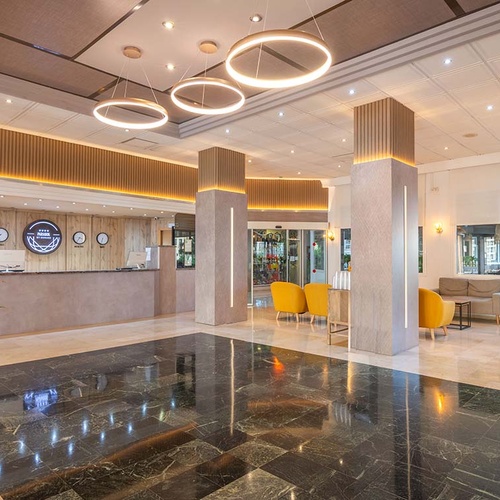 Un moderno y elegante vestíbulo de hotel con un mostrador de recepción, suelos de mármol pulido, lámparas circulares distintivas y cómodas zonas de asiento.