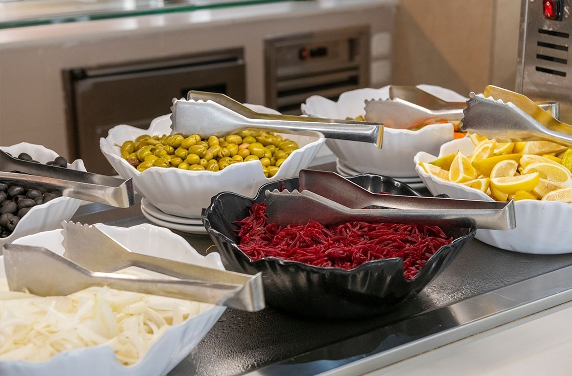 a buffet line with bowls of vegetables and tongs