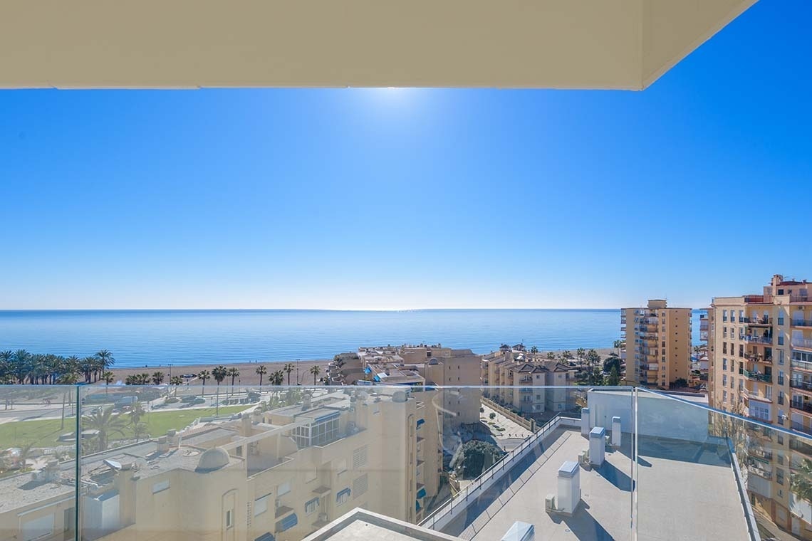 Una vista panorámica desde un balcón que muestra el mar azul, una playa, edificios costeros y un cielo despejado.