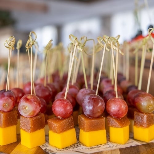 un montón de pinchos de queso y uvas están sobre una tabla de madera