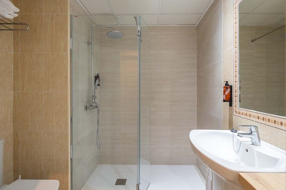 Un baño moderno y funcional con ducha de cristal, lavabo, inodoro y azulejos en tonos neutros.