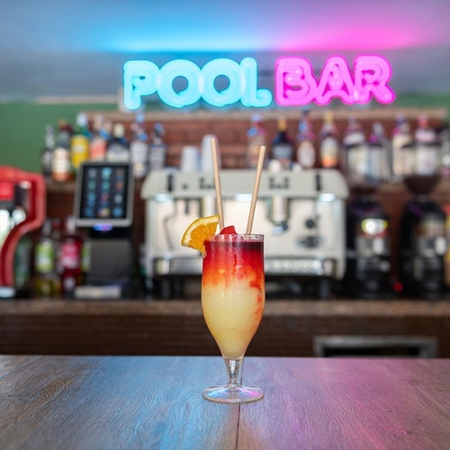 a drink in front of a neon sign that says pool bar