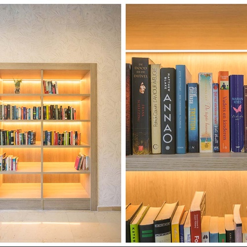 Una estantería de madera empotrada con iluminación LED cálida y llena de libros se integra en una pared con papel pintado de motivos vegetales.