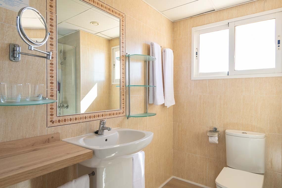 Un baño limpio y bien iluminado con azulejos beige, un lavabo con un espejo grande, un inodoro y una ventana.