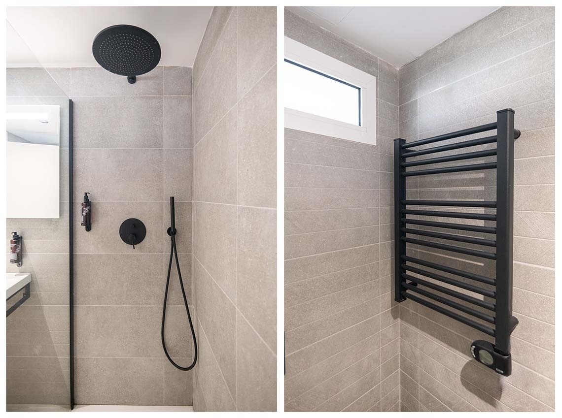 La imagen muestra un baño moderno con azulejos grises, una ducha negra con rociador de techo y de mano, y un radiador toallero negro, complementado por una pequeña ventana.