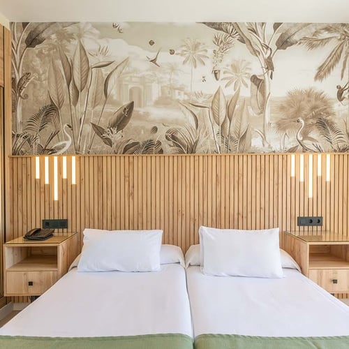 Un dormitorio moderno con dos camas individuales, un cabecero de madera con iluminación integrada y un mural tropical con motivos de jungla y animales.