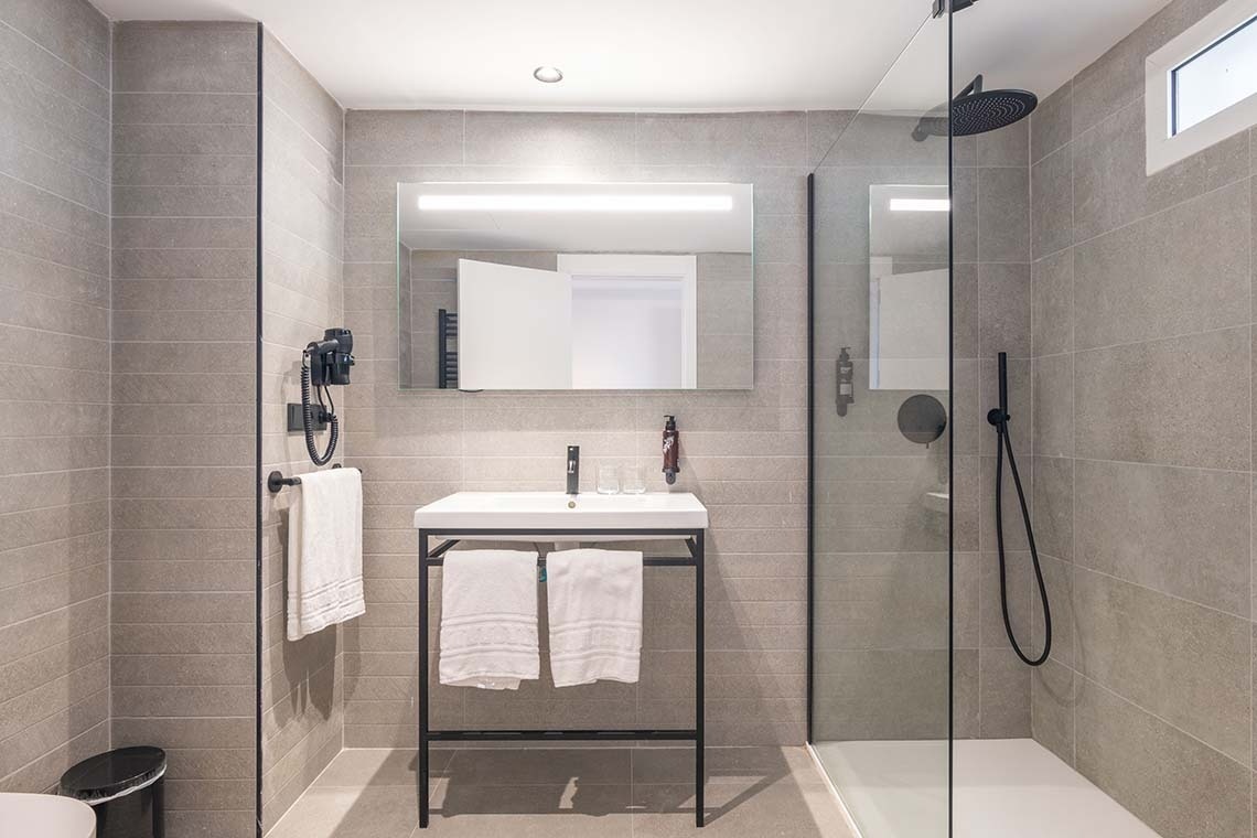 Un baño moderno y elegante con paredes de azulejos grises, un lavabo con un espejo iluminado y una ducha acristalada.