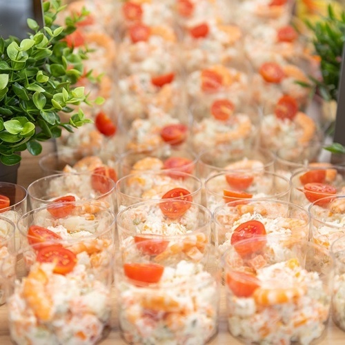 a display of salads with shrimp and tomatoes in plastic cups