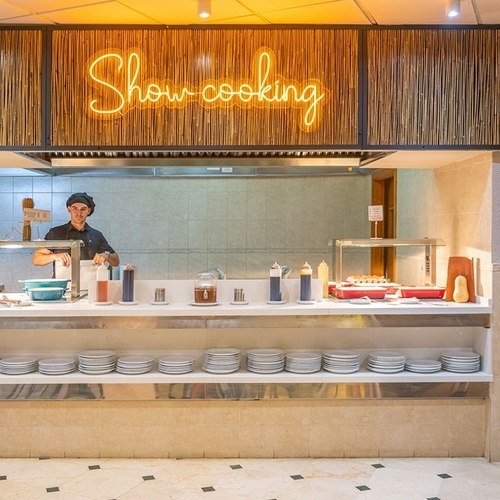 un chef prepara comida en una cocina con un letrero de neón que dice show-cooking