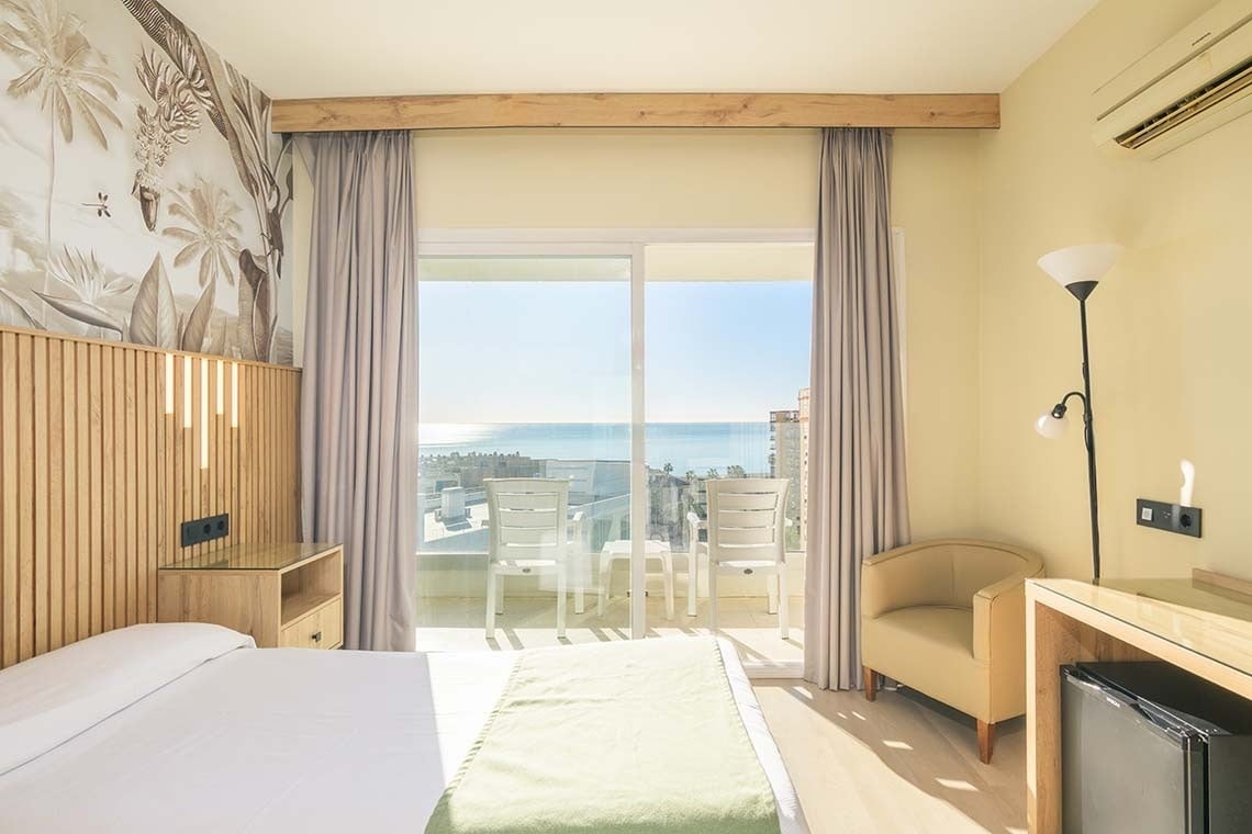 Una habitación de hotel luminosa con balcón que ofrece vistas panorámicas al mar.