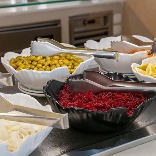 a buffet line with bowls of vegetables and tongs