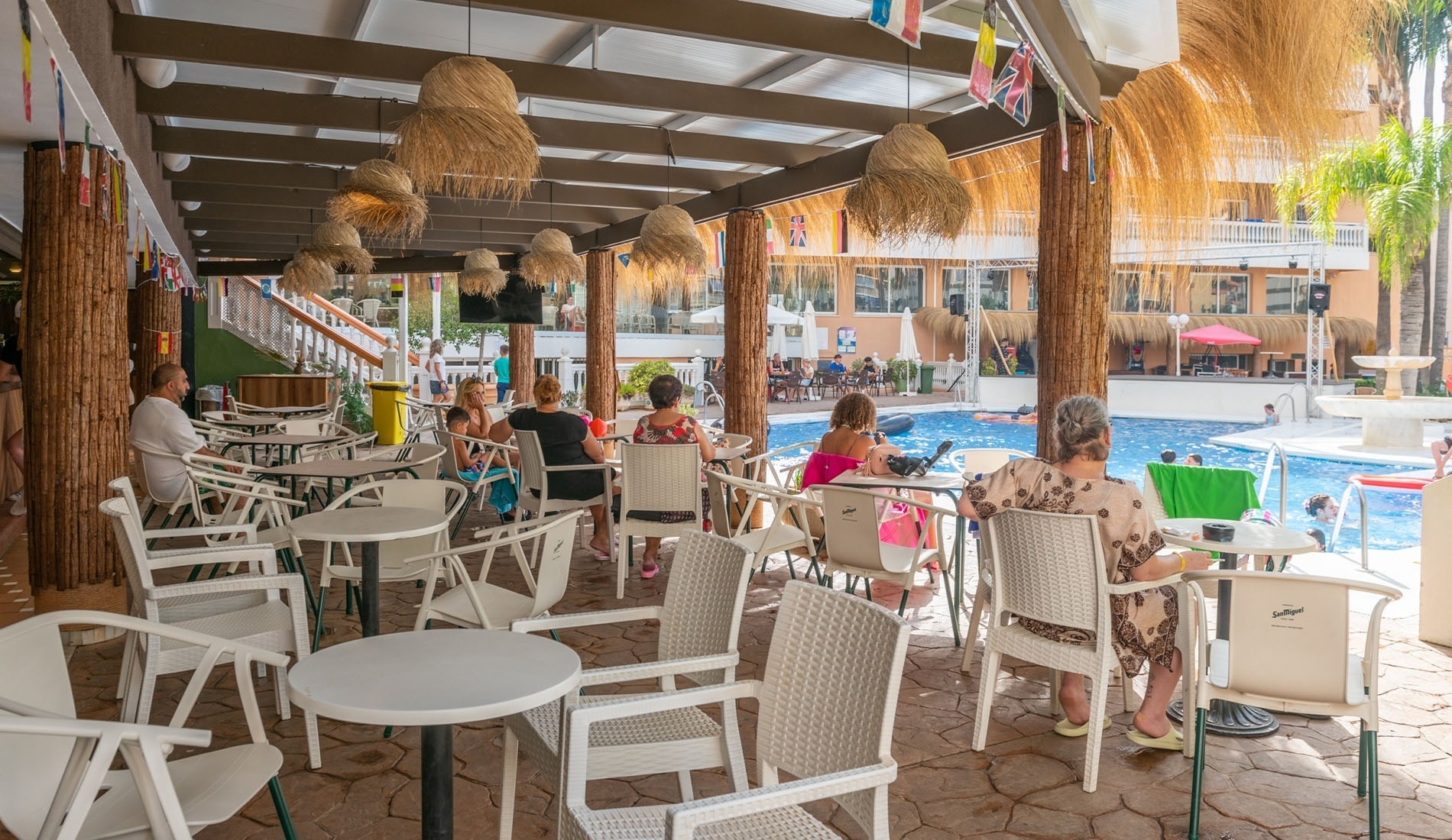 un grupo de personas se sienta en mesas y sillas junto a una piscina