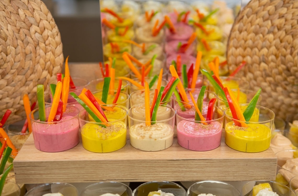 a variety of dips and vegetables in small glasses on a table