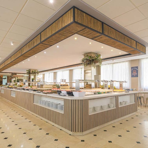 Un amplio y luminoso restaurante tipo buffet con una isla central de comida y una decoración moderna con acentos de madera y bambú.