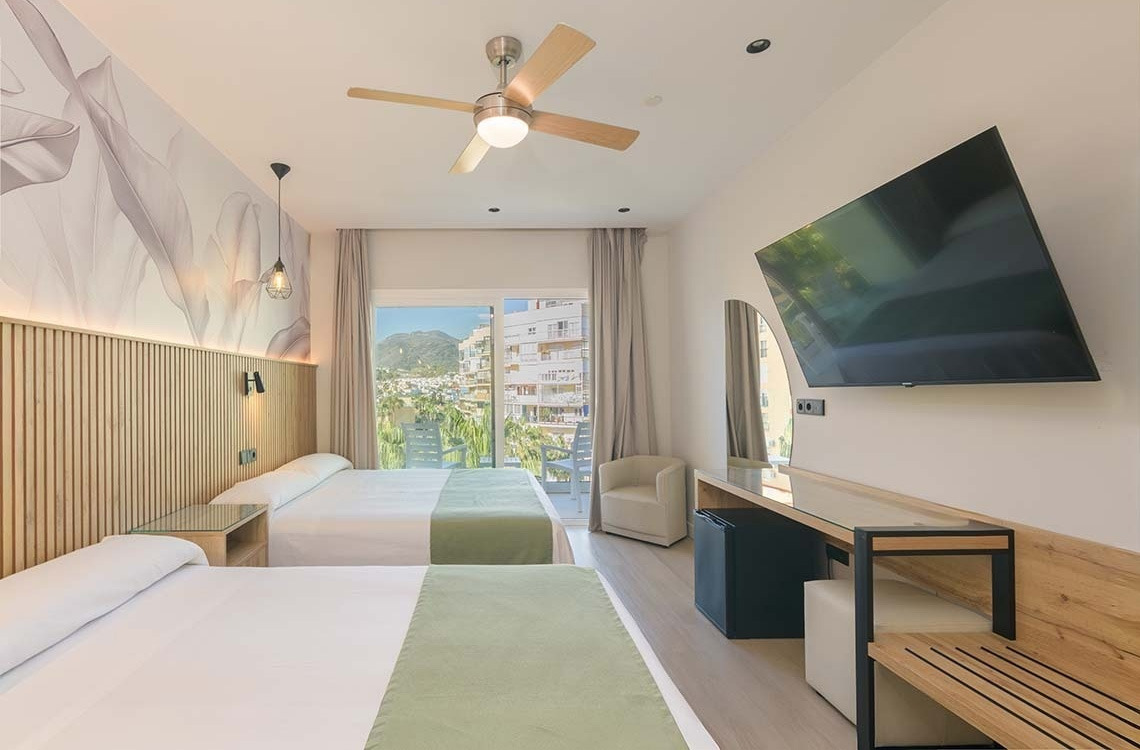 Modern hotel room with two beds, wall-mounted TV, and balcony view. Dorobe: Parasol