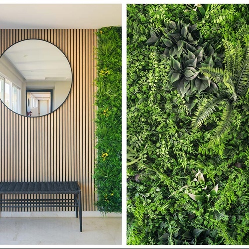 La imagen muestra un recibidor moderno con una pared de listones de madera, un espejo redondo y un banco negro, flanqueado por un vibrante jardín vertical de plantas verdes.
