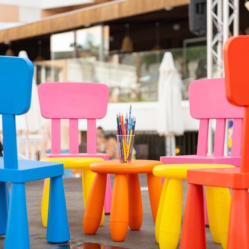 Sillas de colores vivos para niños y una mesa con lápices están dispuestas al aire libre.