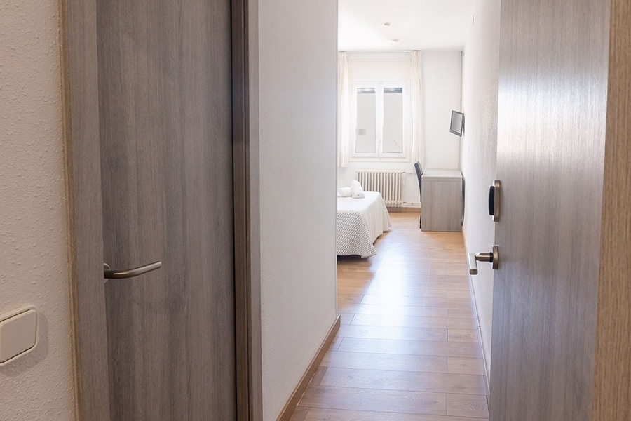 a hallway leading to a bedroom with two beds and a desk