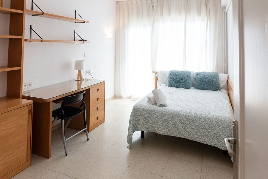 a bedroom with a desk and a bed with blue pillows