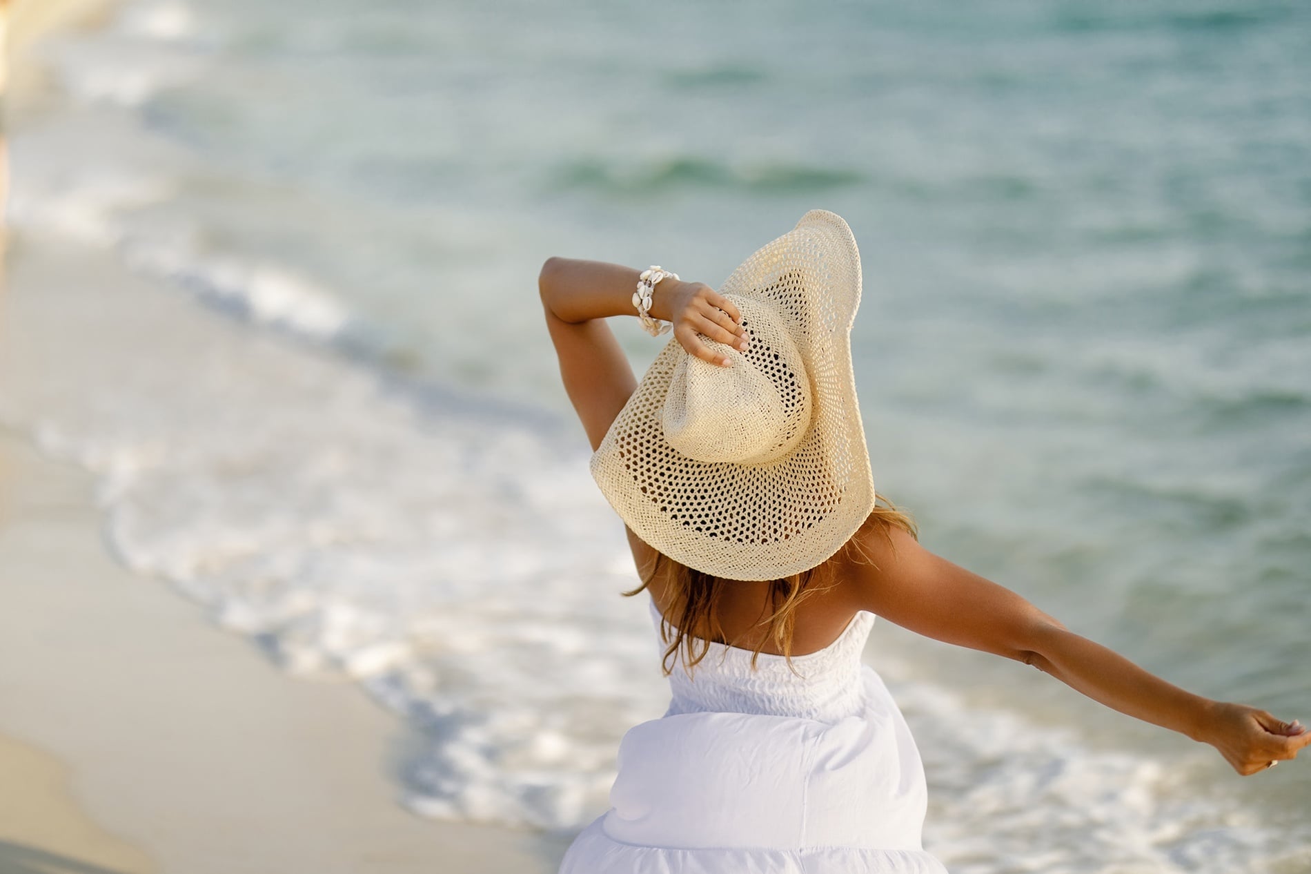 Disfruta la playa desde tu habitación en Hotel Planas: mujer con sombrero blanco y vestido en la orilla.