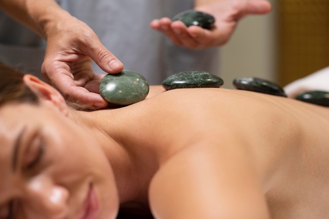 a woman is getting a massage with green rocks on her back