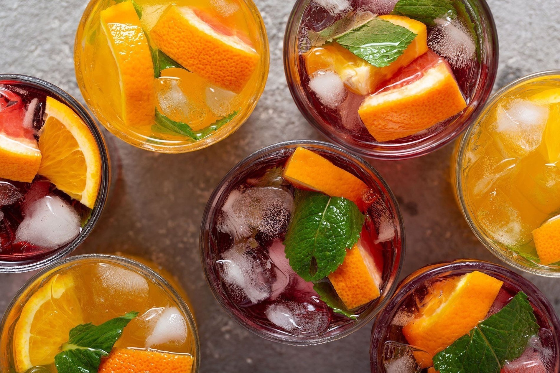 several glasses of iced drinks with orange slices and mint leaves