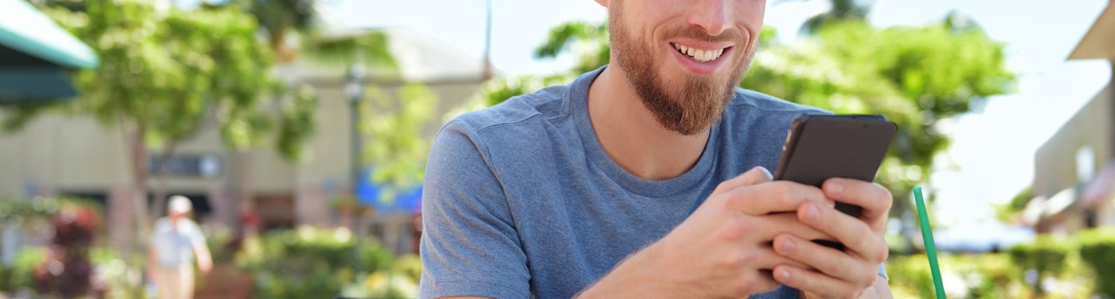 un hombre sonríe mientras usa su teléfono inteligente en un parque .