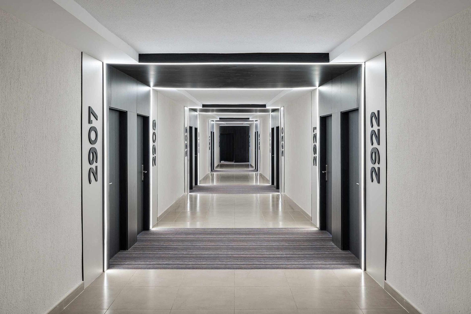 Le couloir d'un hôtel moderne est éclairé par des bandes LED linéaires qui accentuent sa symétrie, ses portes sombres et sa perspective fuyante.