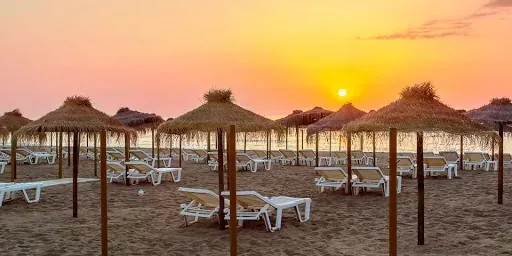 Sunset at Hotel Puente Real Torremolinos beach with umbrellas and loungers.