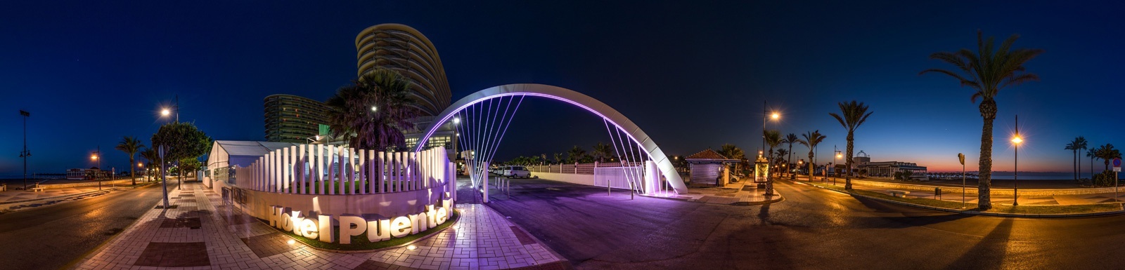 une vue panoramique d' un pont la nuit avec des palmiers et un bâtiment en arrière-plan .