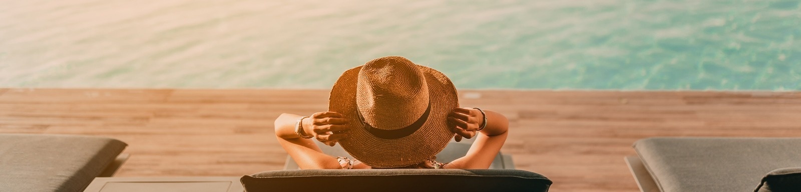 une femme portant un chapeau est assise à côté d' une piscine