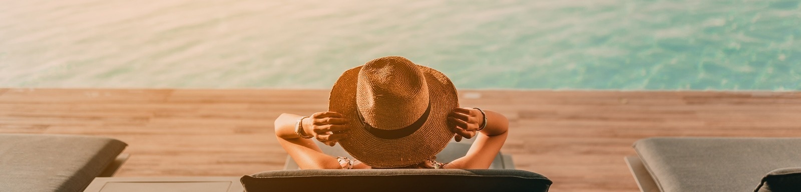 a woman wearing a hat sits in a chair by a pool